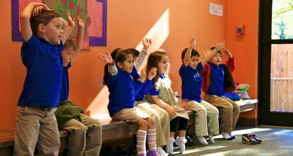 Children sitting on a bench with hands raised