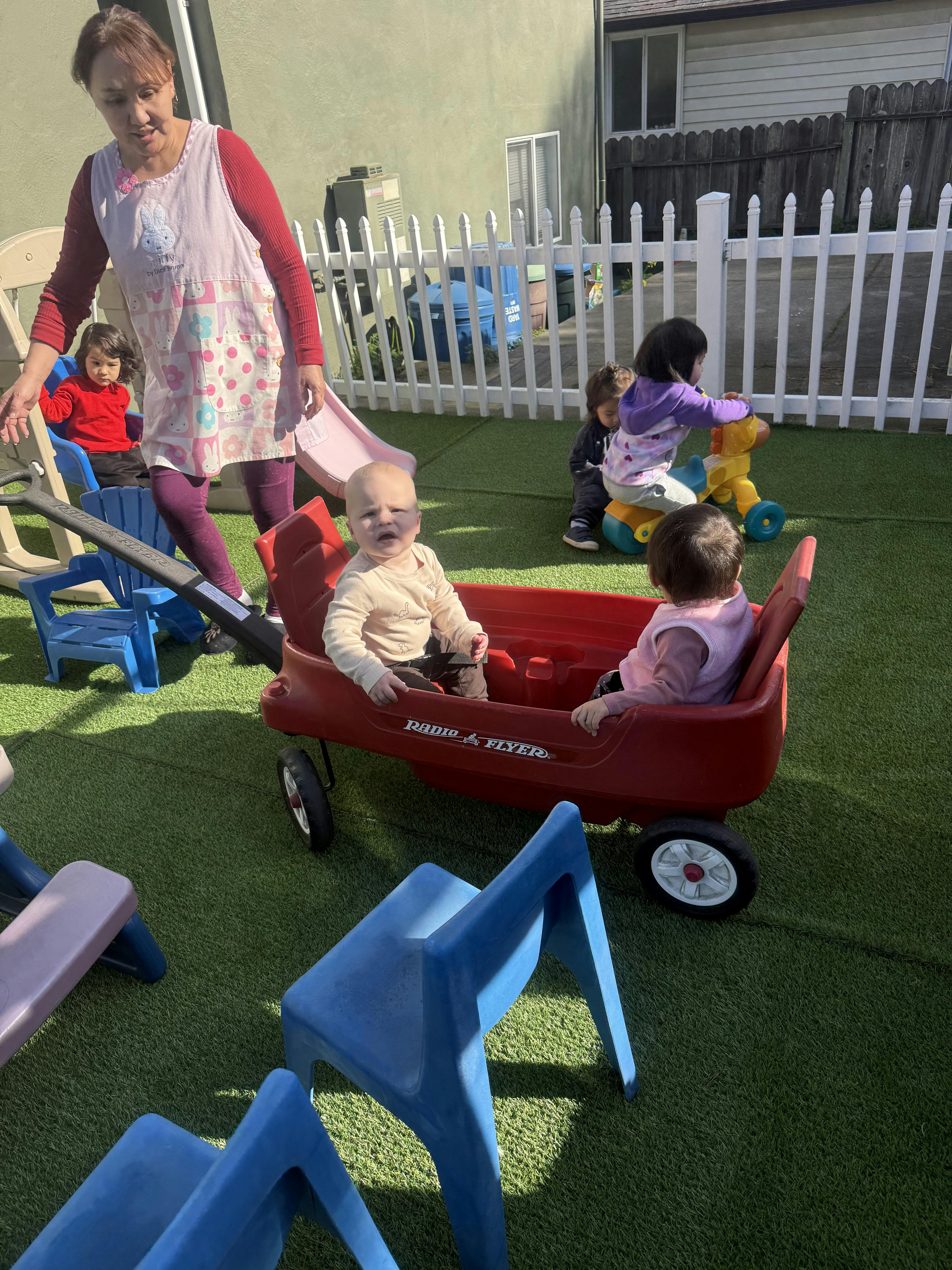 Adult pulling a wagon with two children, other children playing in background