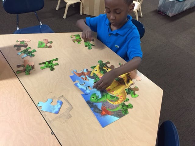 Child in a blue shirt assembling a puzzle on a table