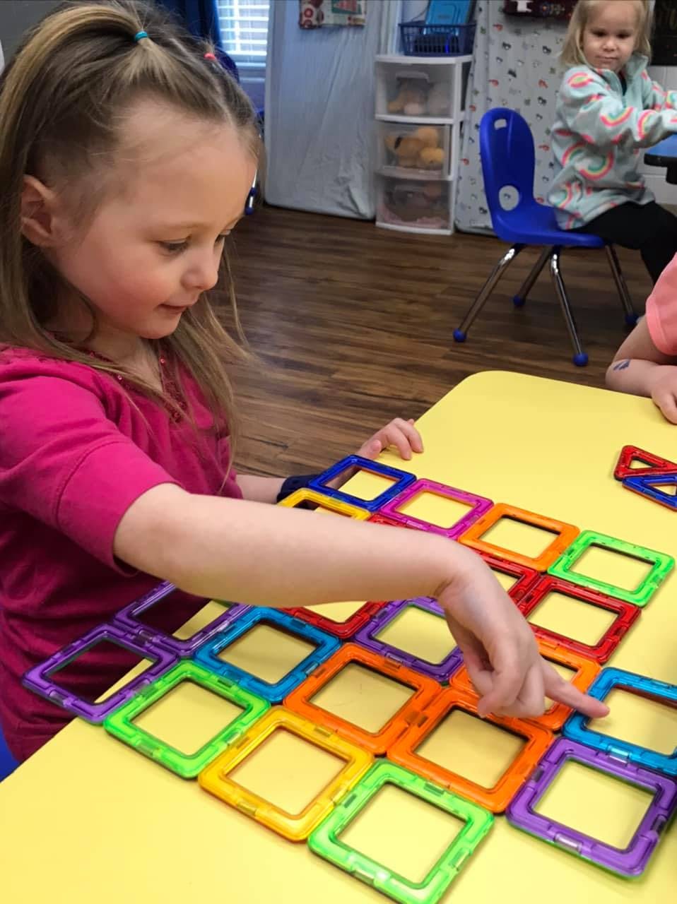 Child playing with colorful magnetic tiles on a yellow table