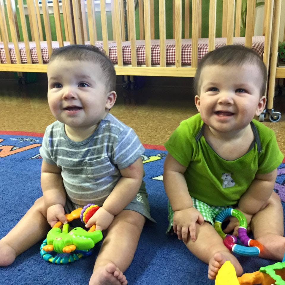 Two children sitting on a rug with toys