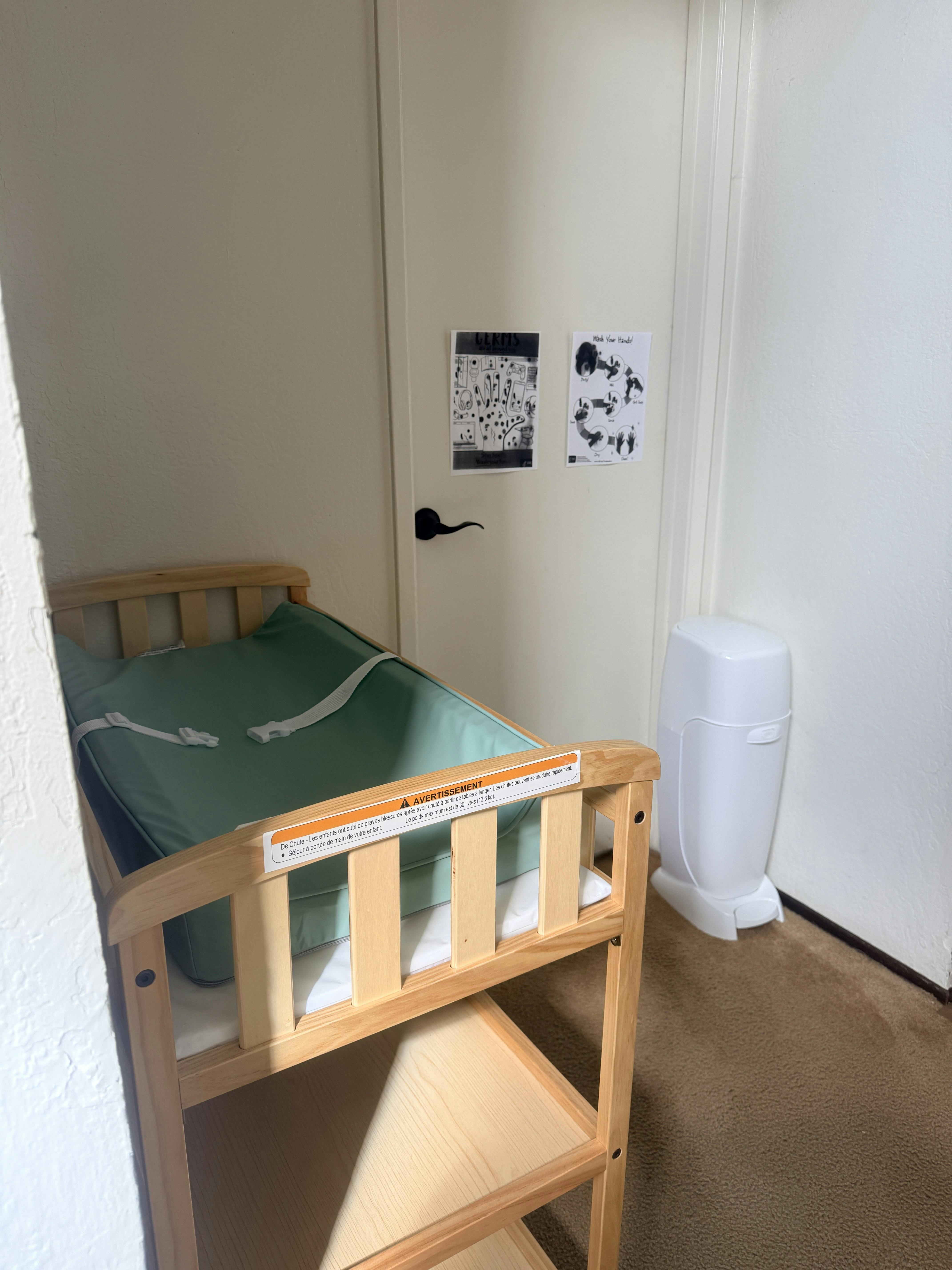 Wooden baby changing table with green pad and diaper disposal bin