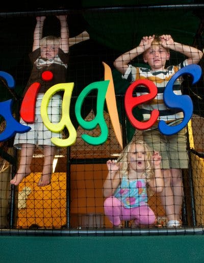 Three children behind a net with colorful letters spelling "Giggles"
