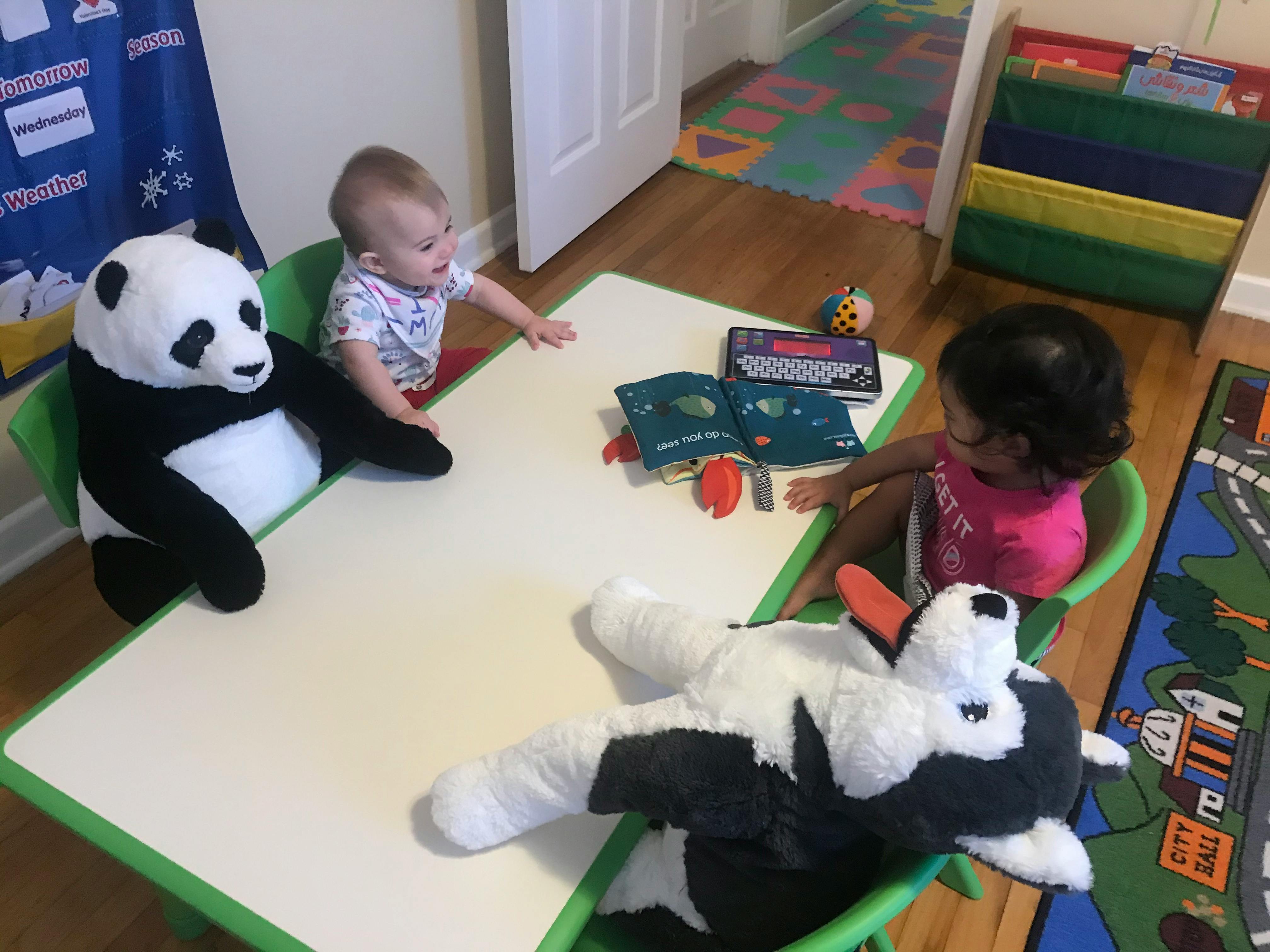Two children and two stuffed animals sitting at a table with books