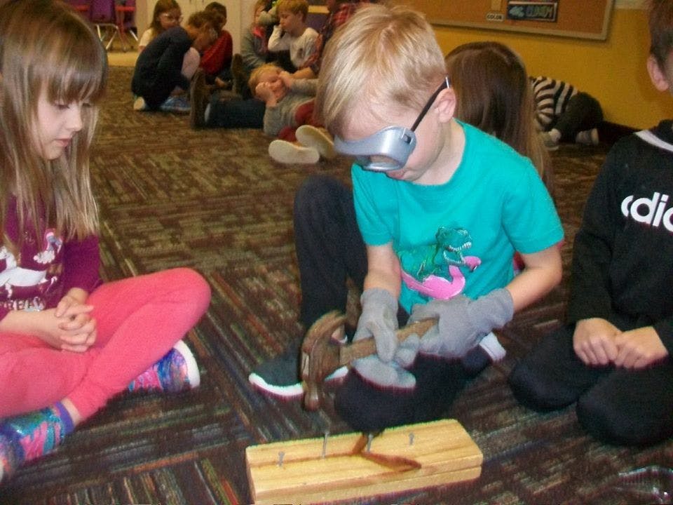 Child wearing goggles and gloves hammering a nail into wood