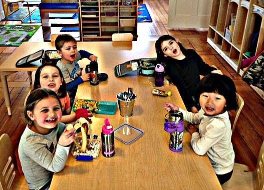 Five children sitting at a table with lunchboxes and water bottles