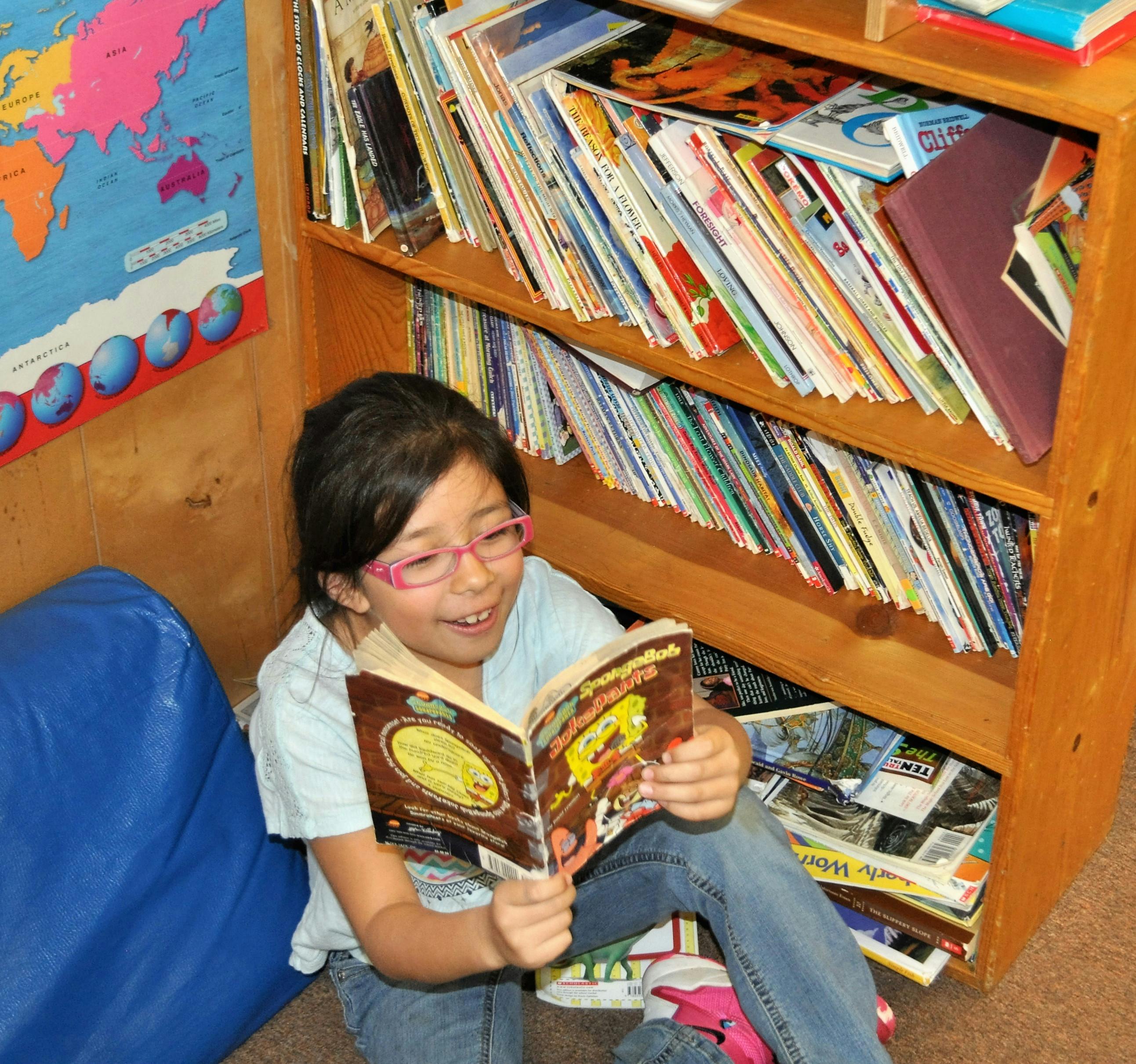Child reading a book in a classroom next to a bookshelf