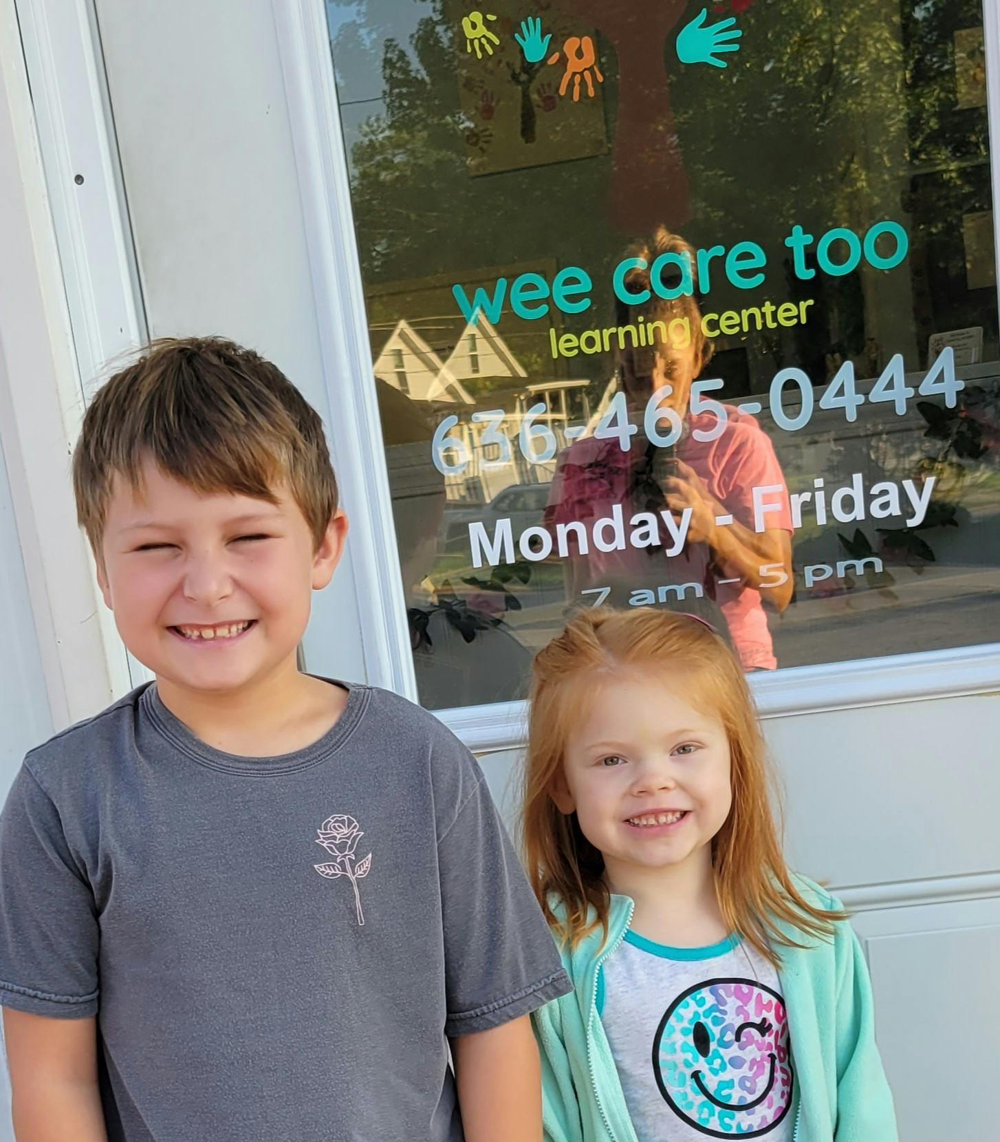 Two children standing in front of a window with "wee care too learning center" text