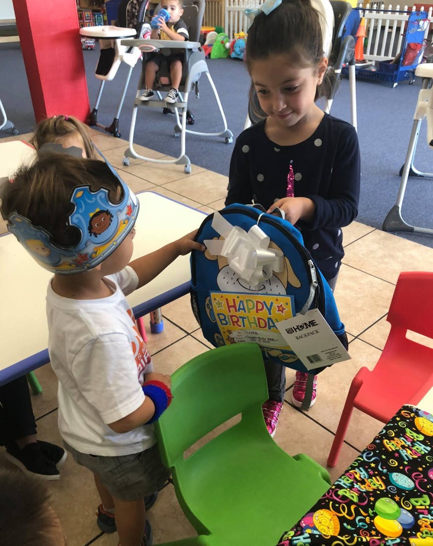 Child in crown reaching for a gift bag held by another child