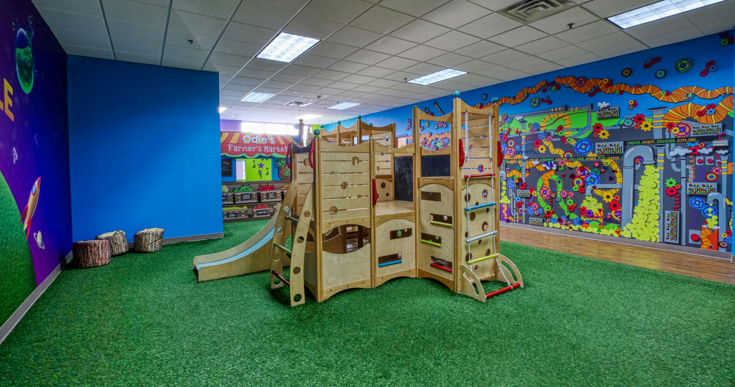 indoor playground with wooden climbing structure and green turf flooring