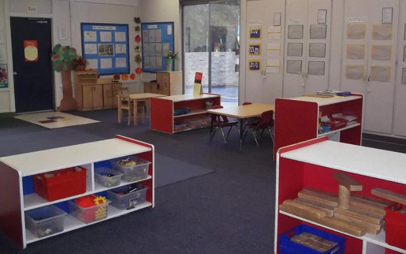 Classroom with child-sized tables and chairs, shelves with toys and learning materials