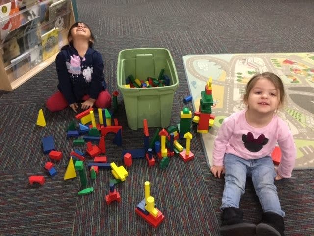Two children playing with colorful building blocks on a carpeted floor