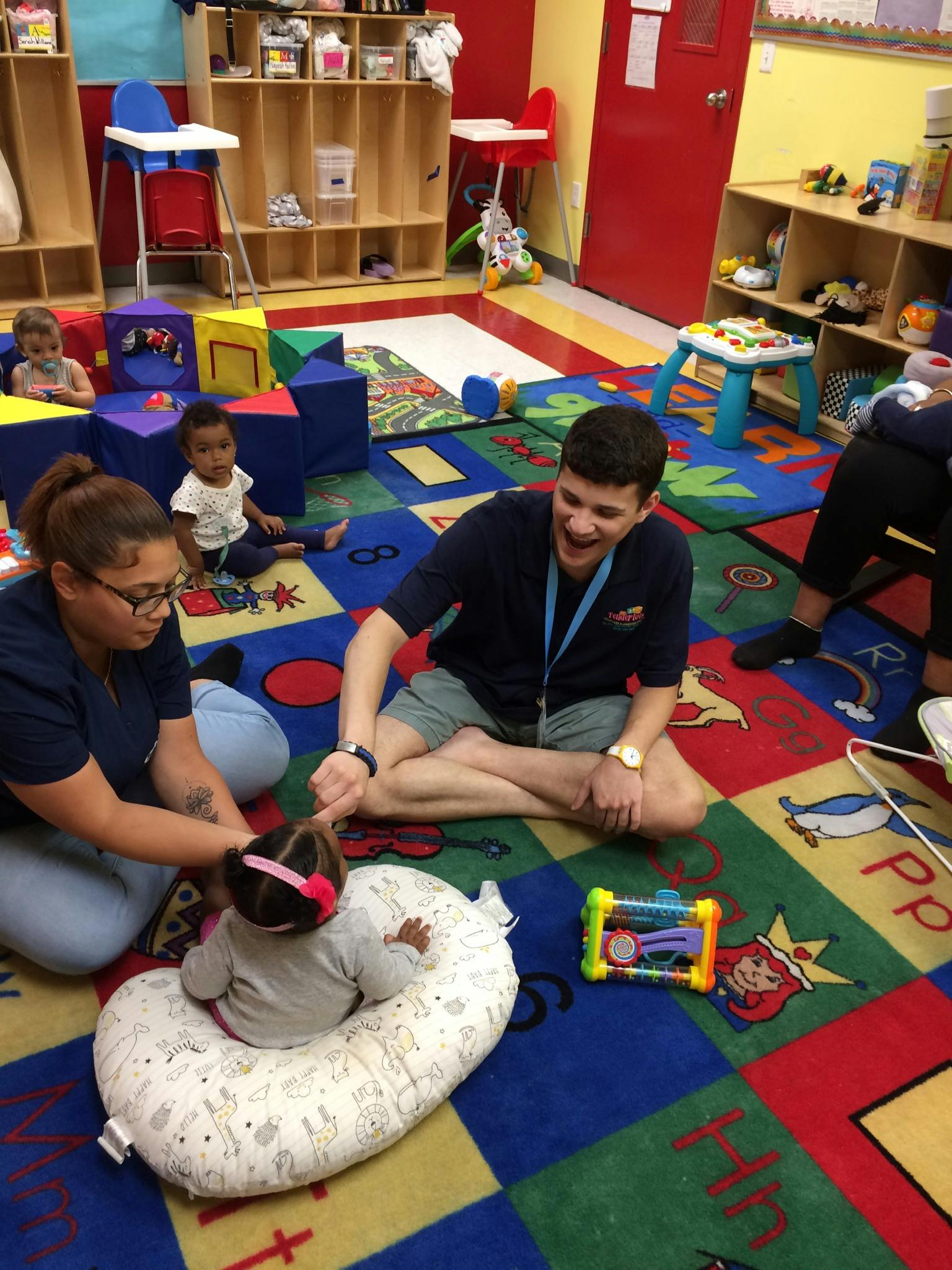 Two adults and three children on a colorful rug in a play area