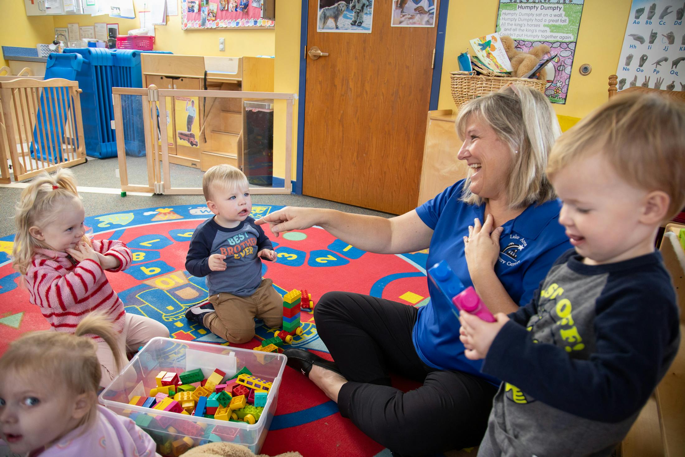 Adult and three children playing with blocks on a colorful rug in a classroom