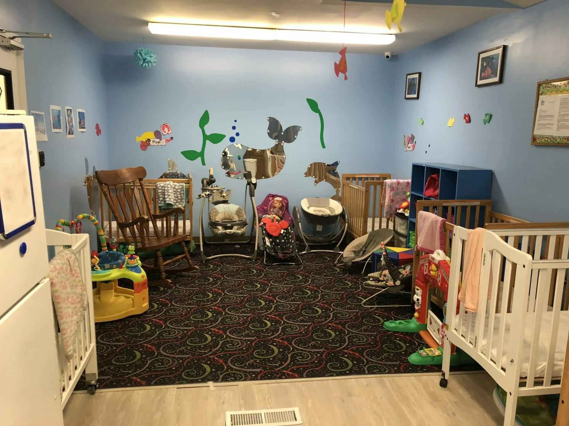 Nursery room with multiple cribs, a rocking chair, and baby swings