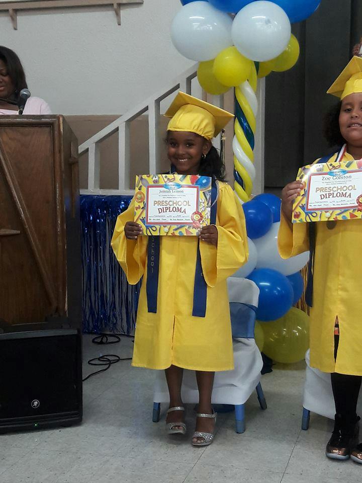 Child in yellow graduation gown holding a preschool diploma