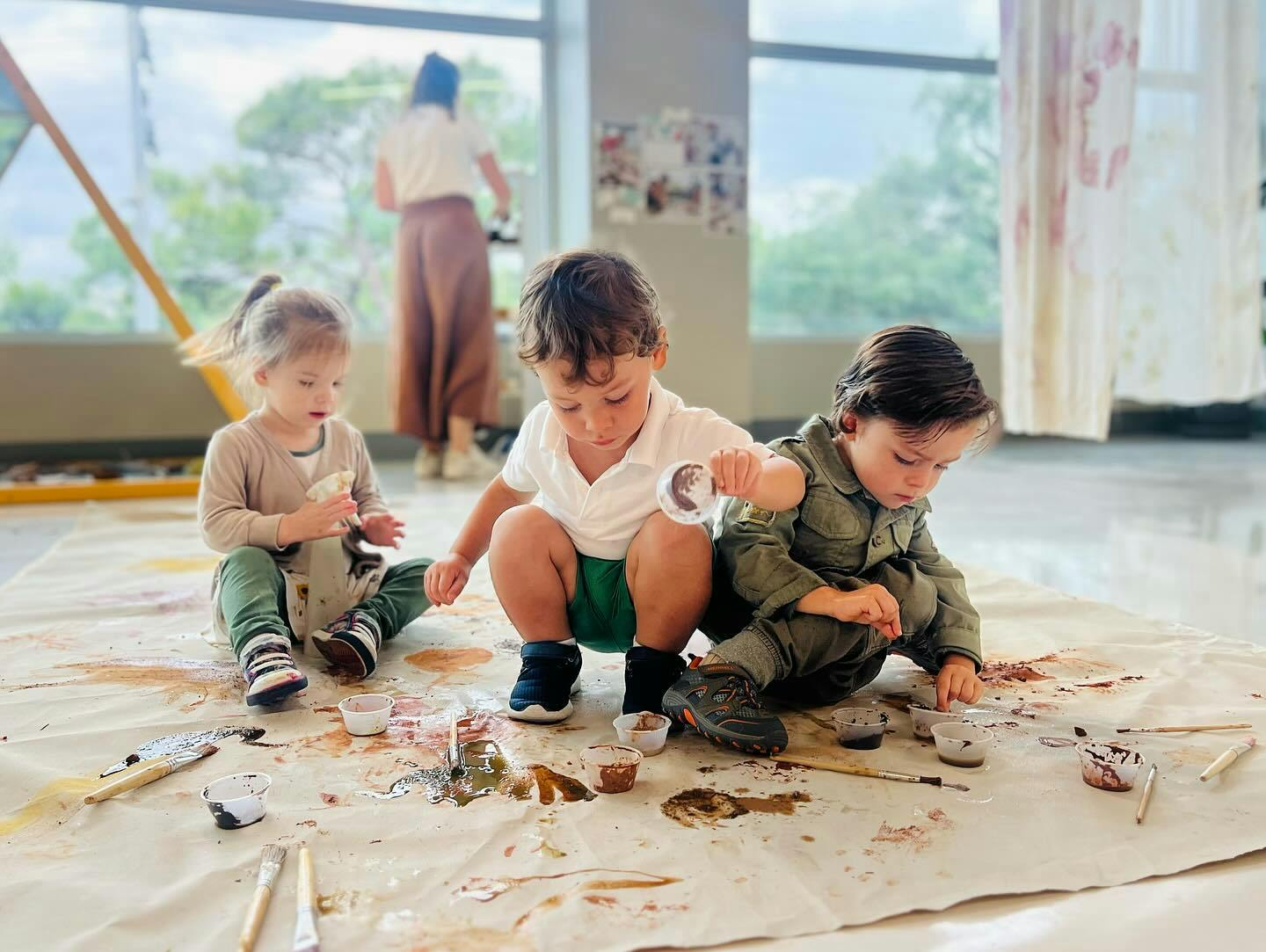Three children painting on a drop cloth