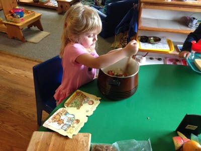Child stirring contents in a pot on a green table