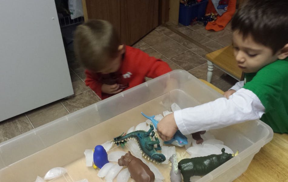 Two children playing with animal toys and ice in a container