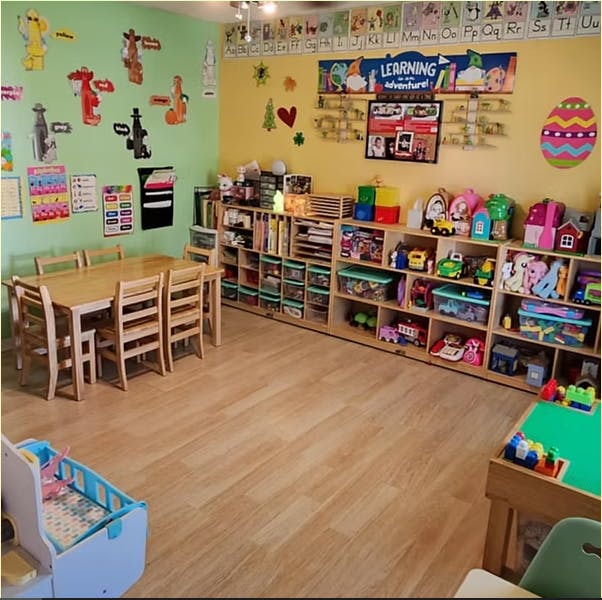Classroom with small wooden tables and chairs, shelves filled with toys and books