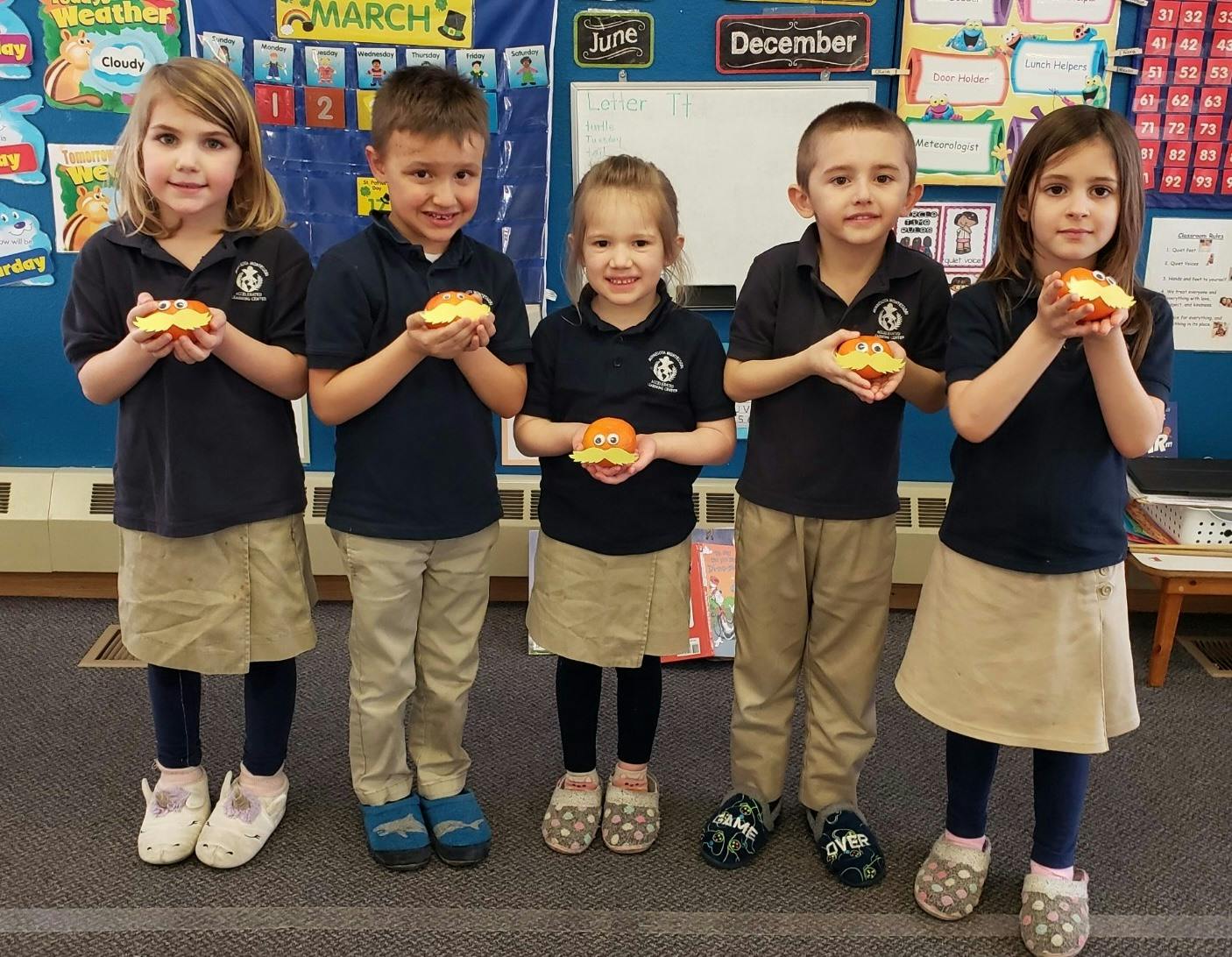 Five children holding small objects in a classroom