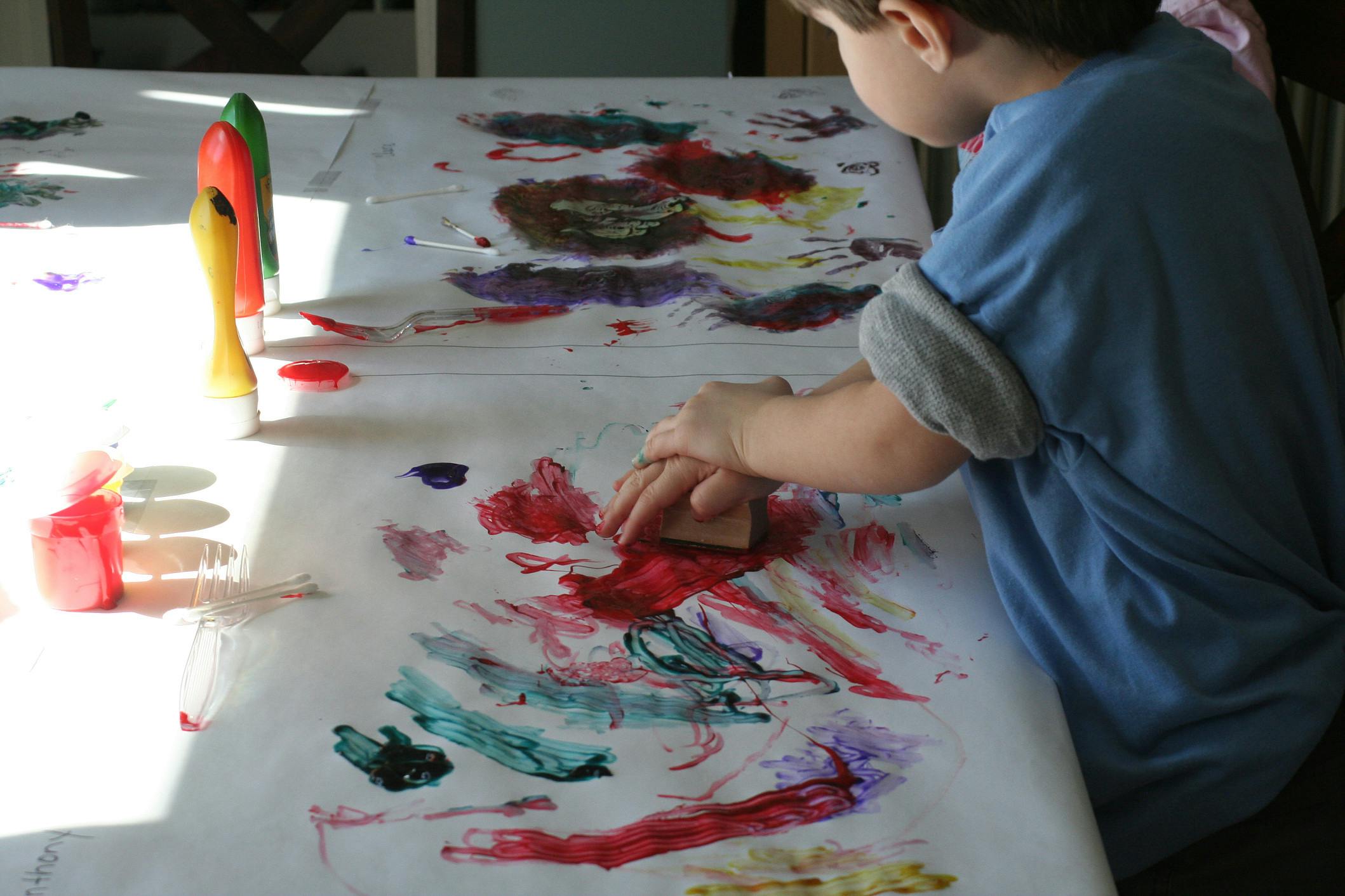 Child painting on a large sheet of paper with a sponge