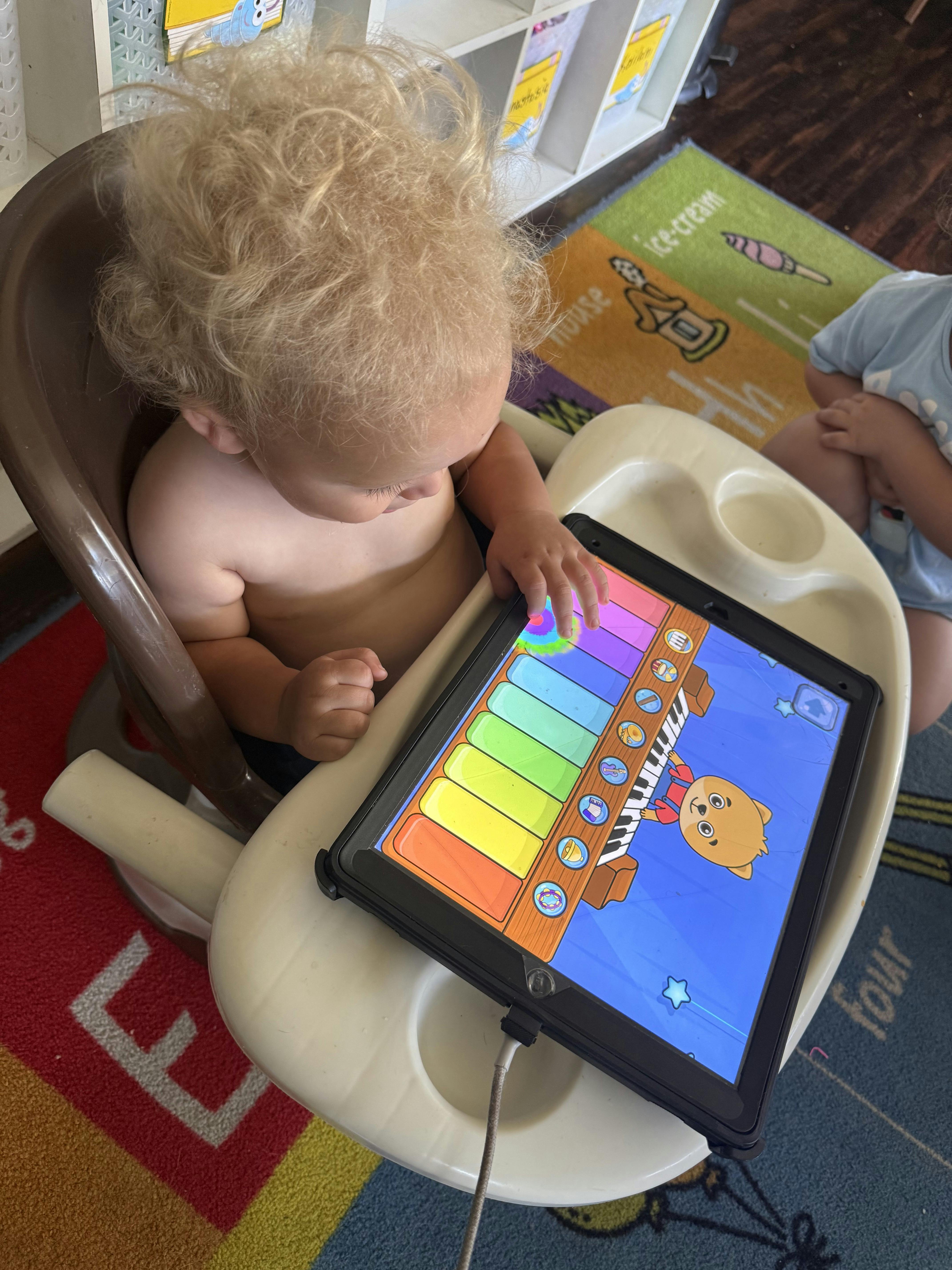 Child in a high chair playing a colorful piano app on a tablet
