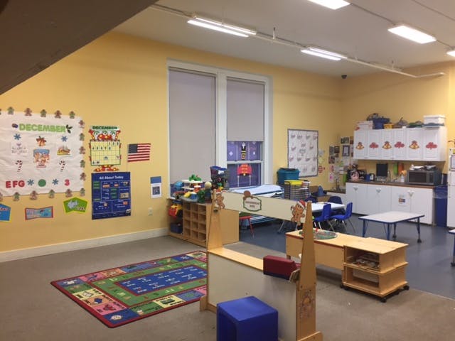 Empty classroom with yellow walls, colorful rug, and various learning materials