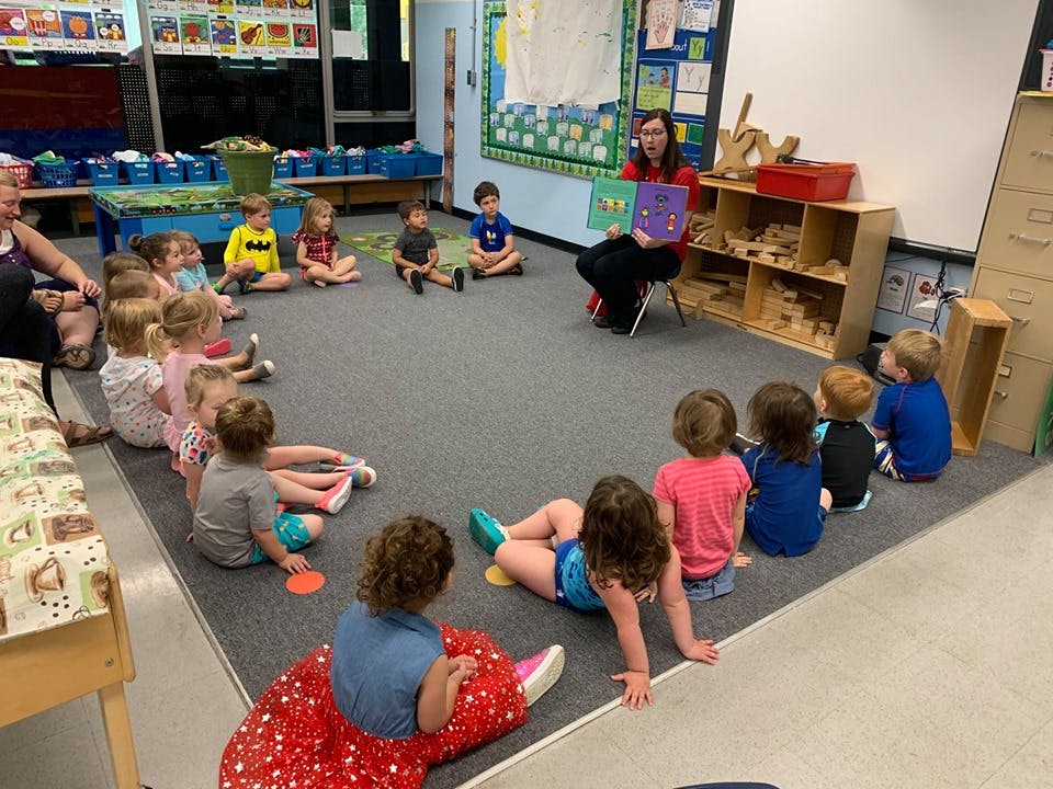 Person reading a book to a group of children in a classroom