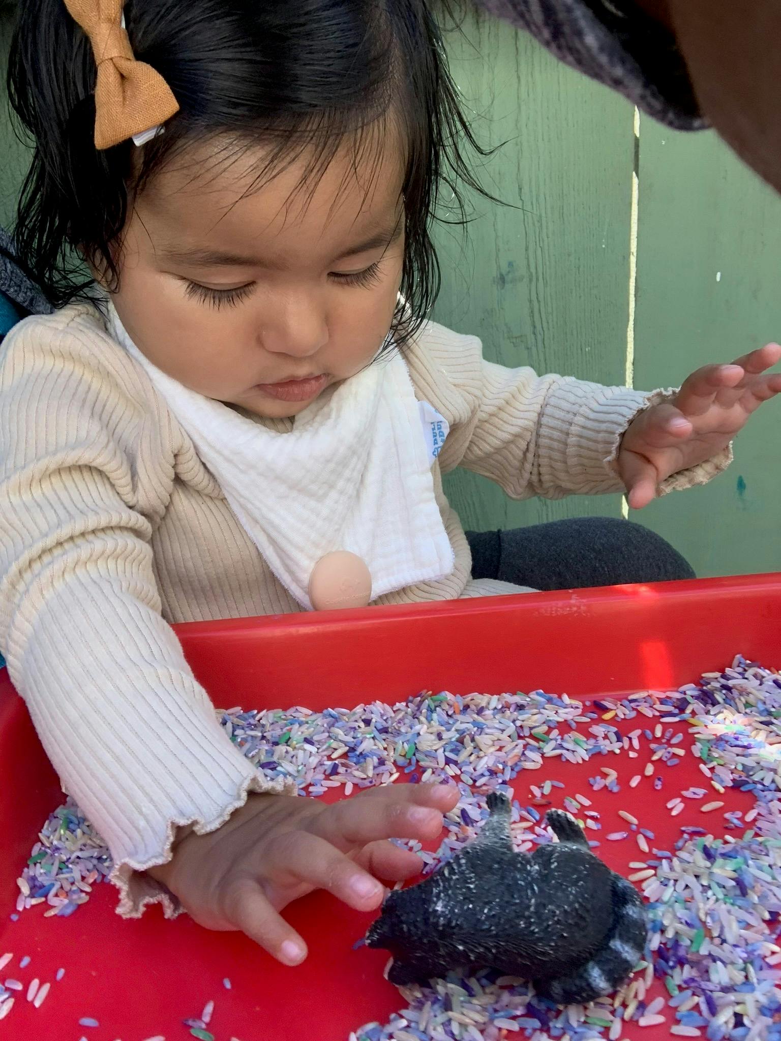 Child playing with rice and a toy in a red bin