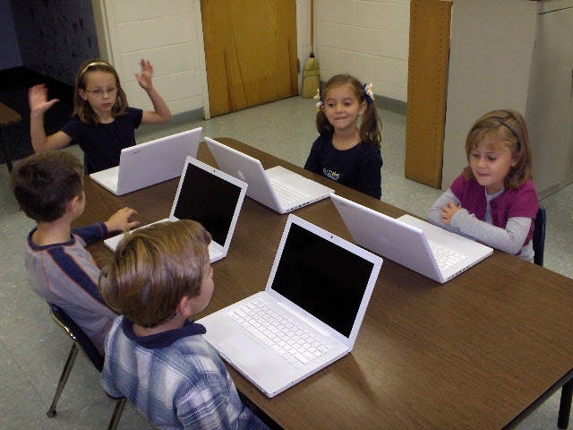 Children sitting at a table with laptops