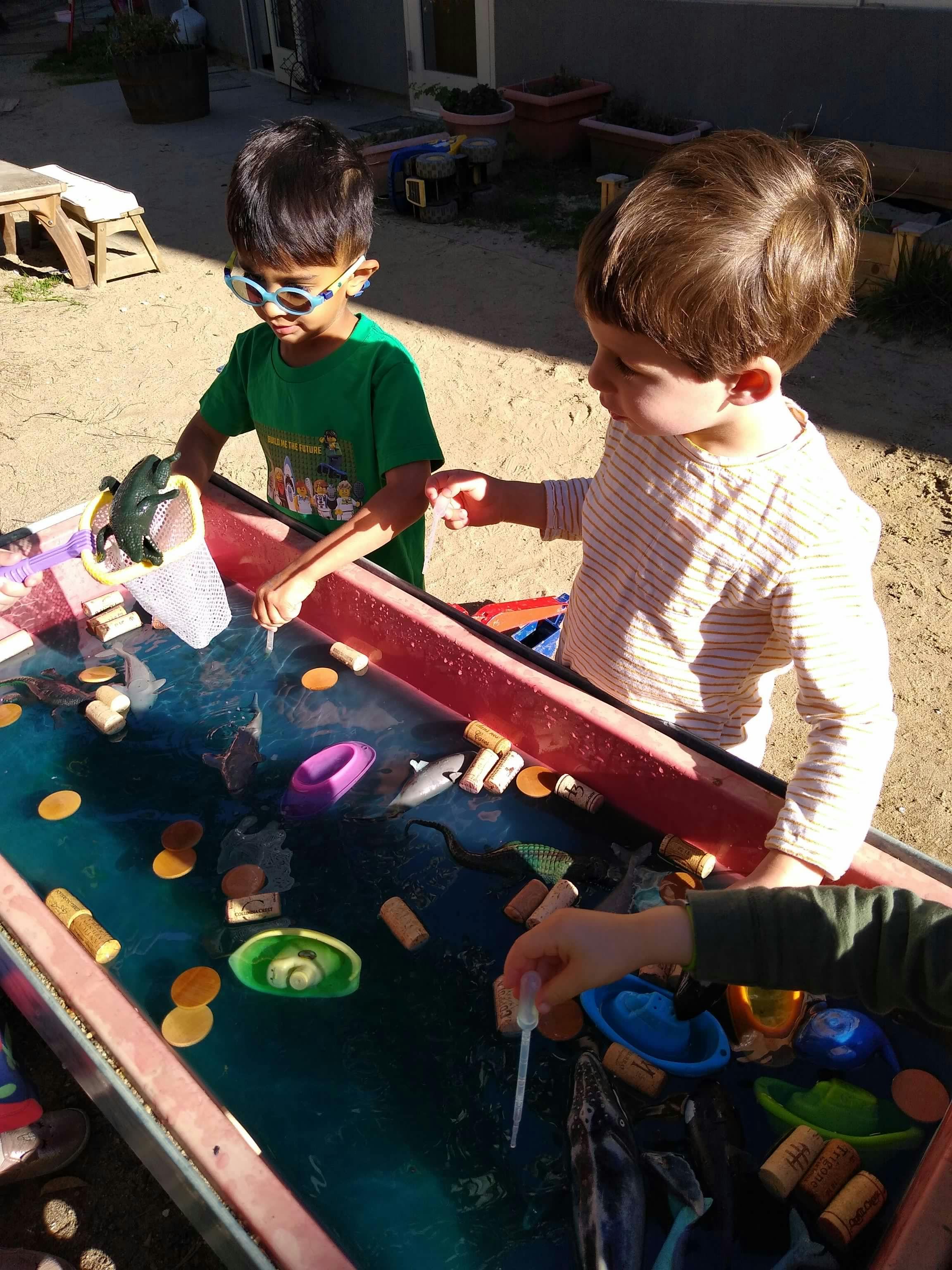 Two children playing at a water table with various objects