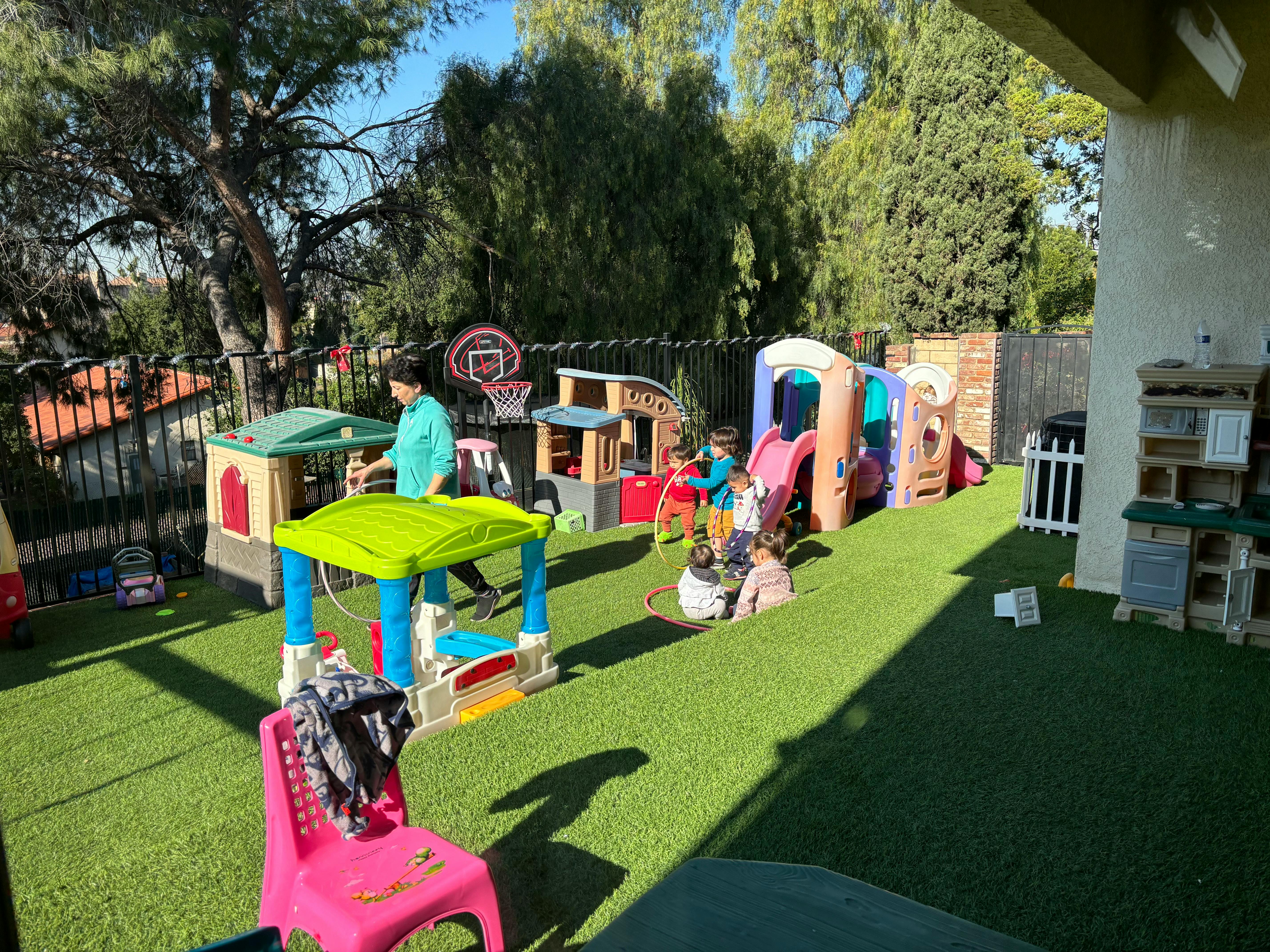 Person and children playing in an outdoor play area with playhouses and slides