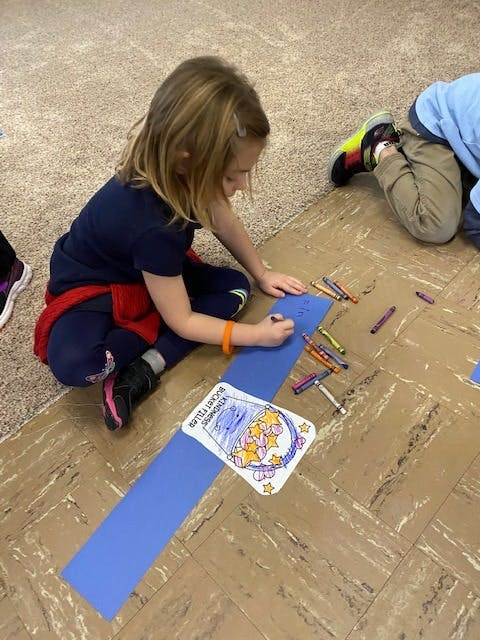 Child coloring on a blue paper strip on the floor