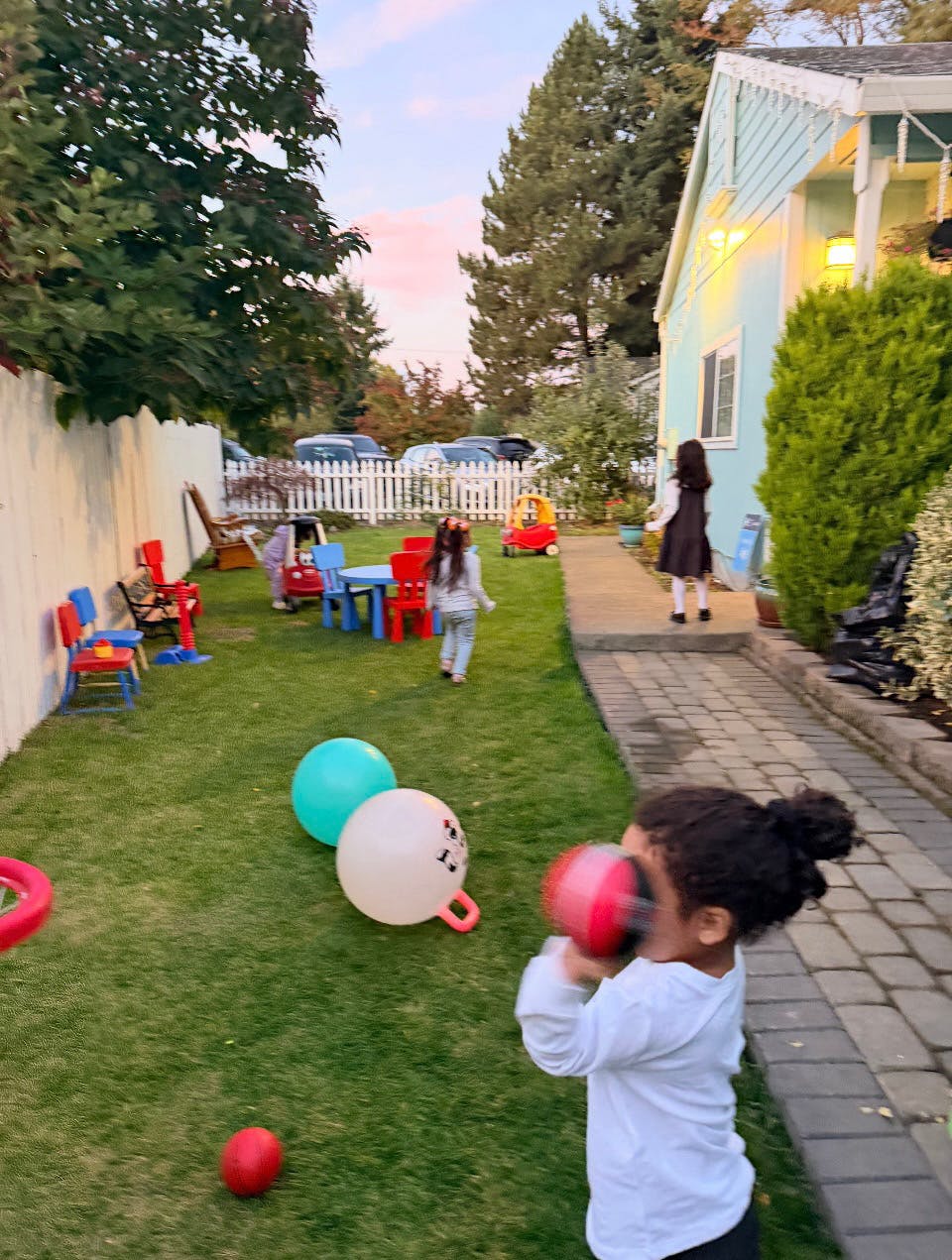 Child in a white shirt holding a red and black ball, other children in the background