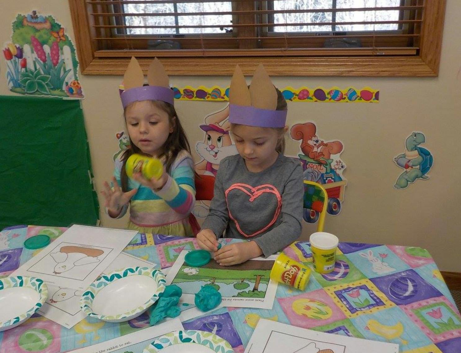 Two children wearing paper crowns playing with modeling clay at a table