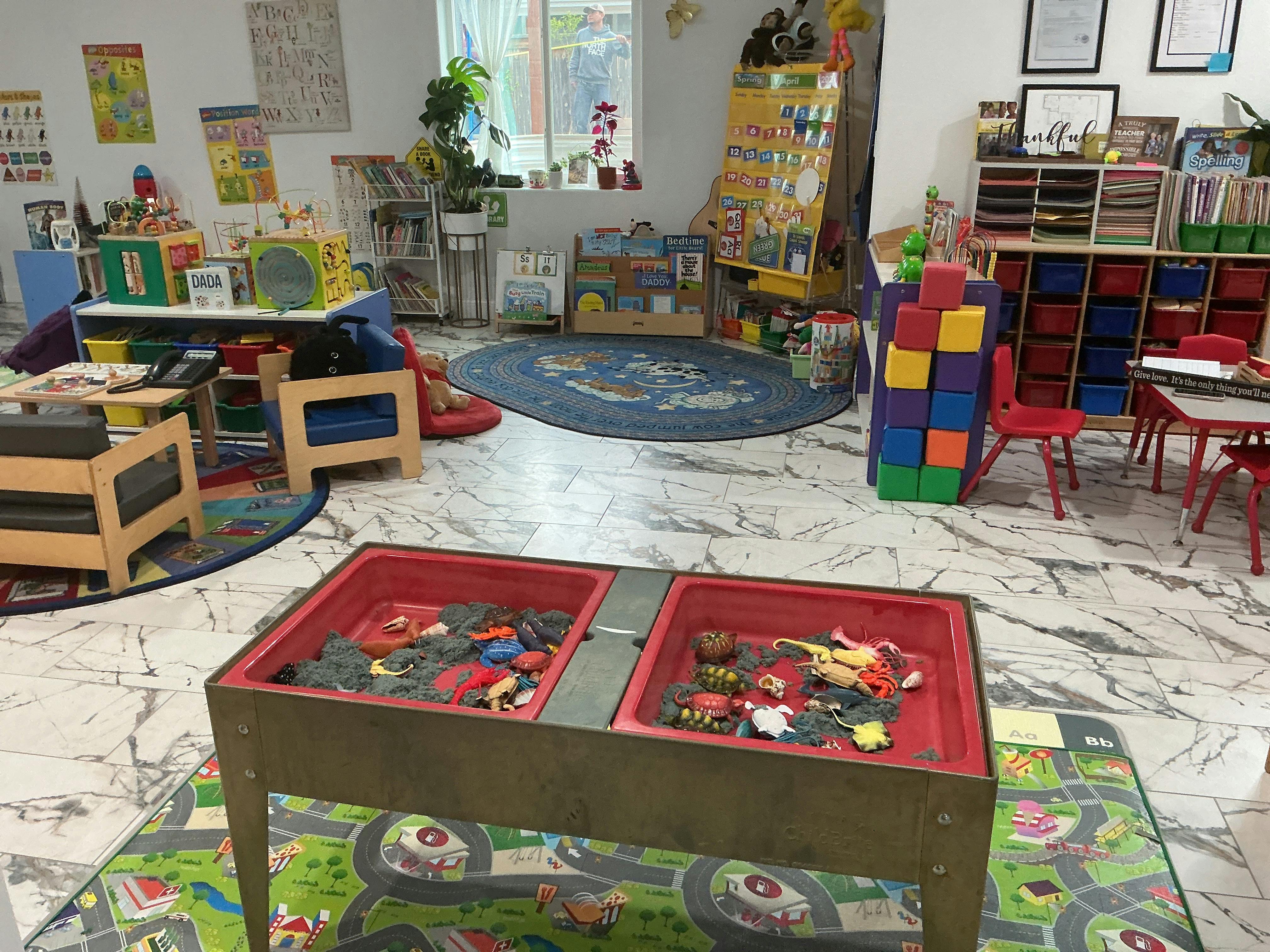 Classroom with sand and water table, small tables and chairs, and educational posters