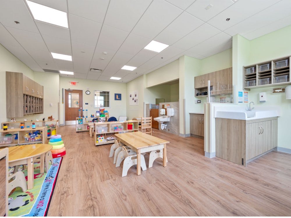 Classroom with small tables, shelves of toys, and a baby changing station