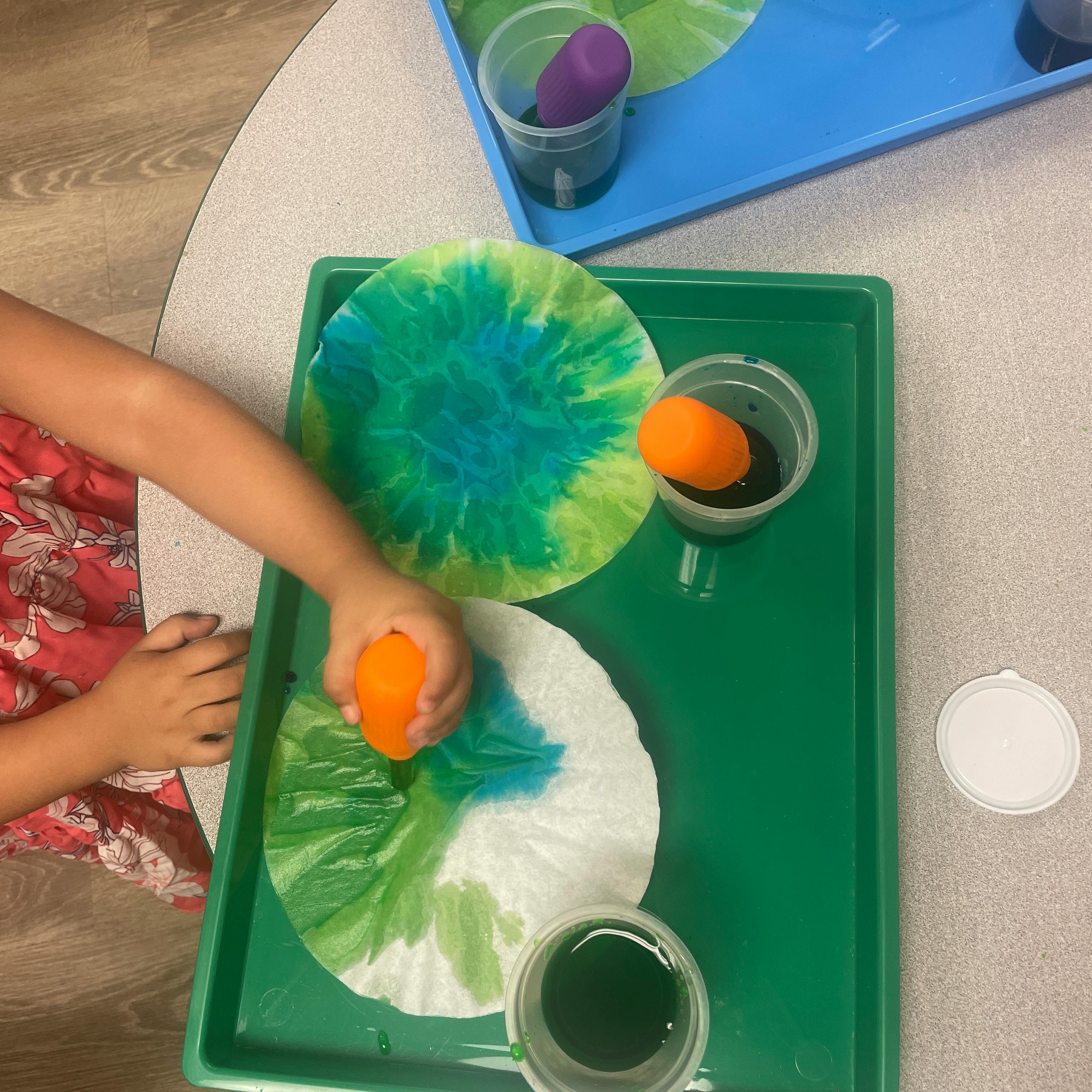 Child's hands coloring coffee filters with sponges and liquid colors