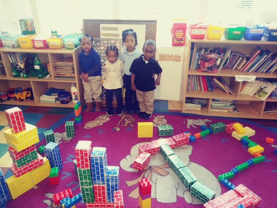 Four children standing in a classroom with block structures on the floor
