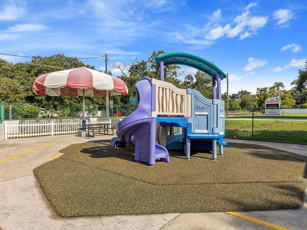 A children's playground with a purple slide and a red and white umbrella