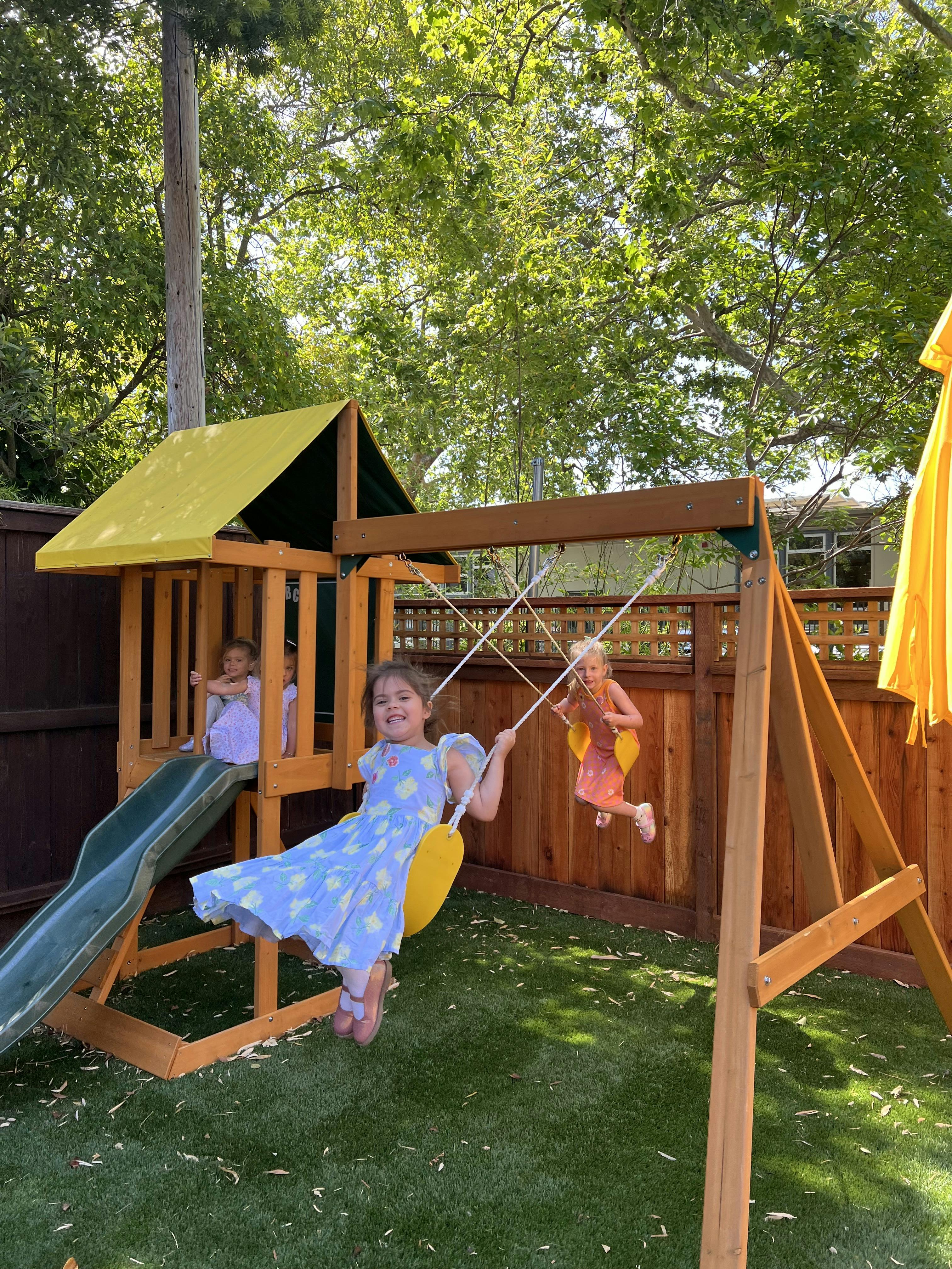 Child on a swing set, another child on a swing, and a child in a playhouse