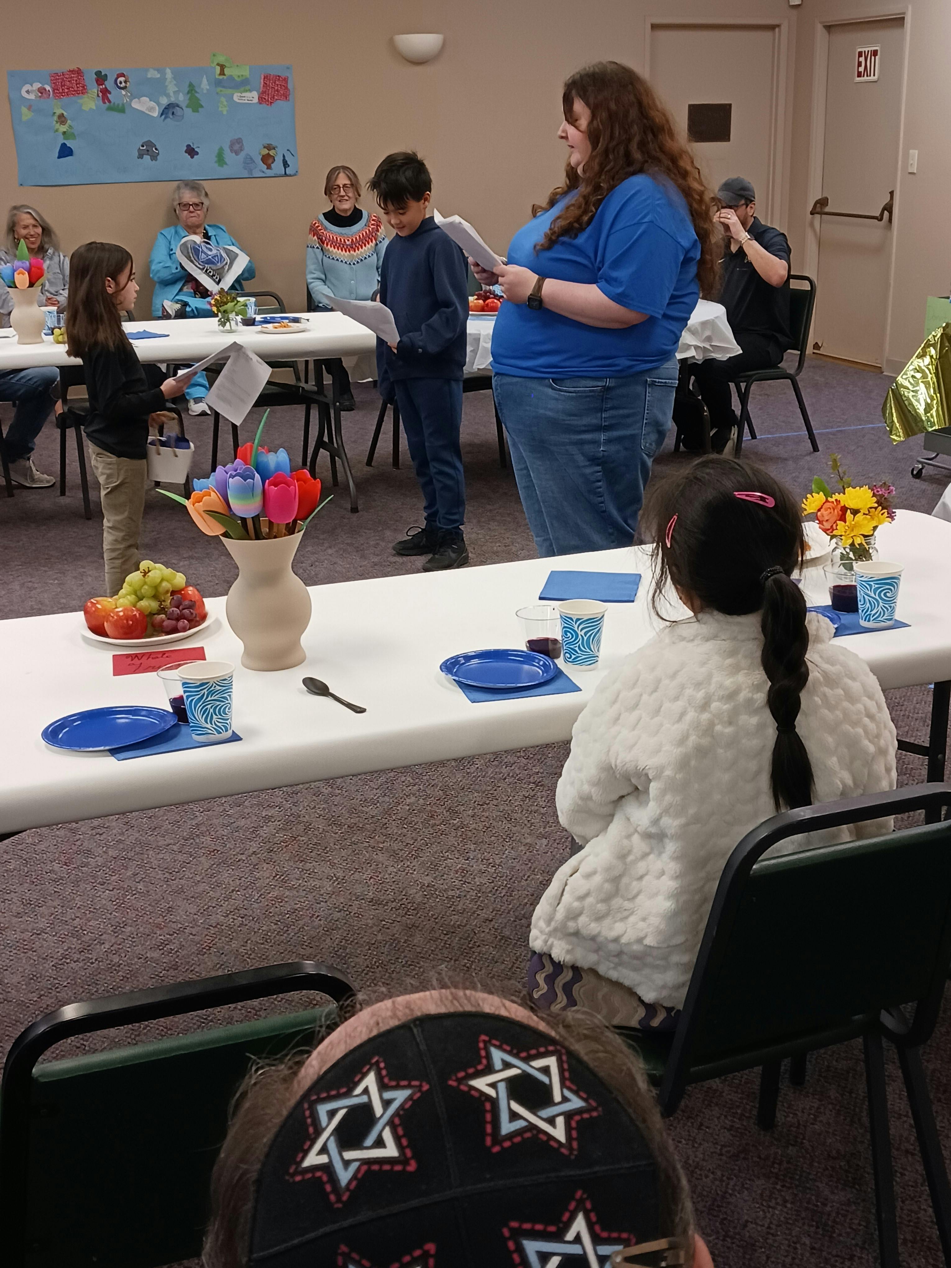 Adult and two children standing and reading from papers in a room with tables