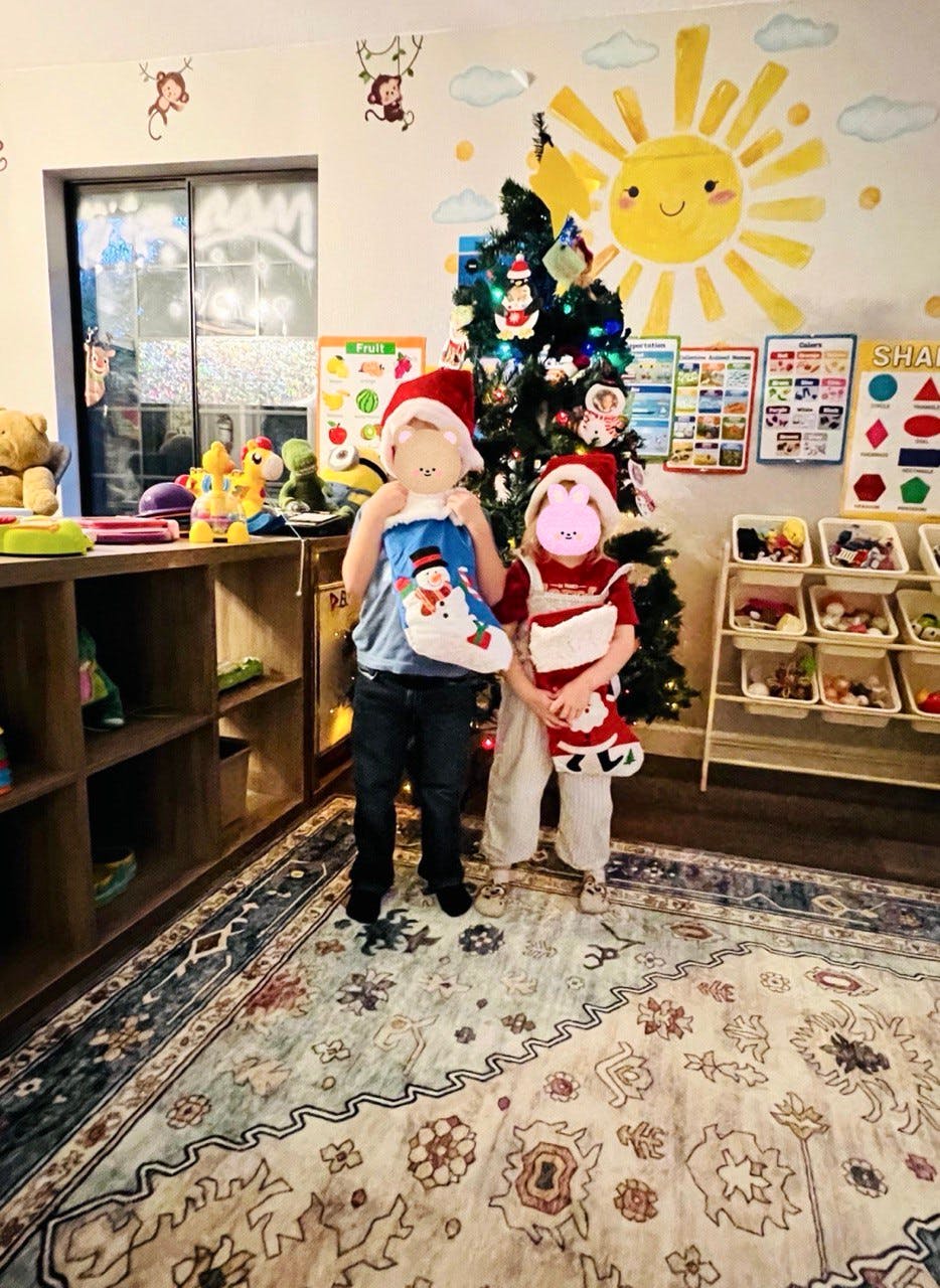 Two children wearing Santa hats and holding Christmas stockings in a classroom