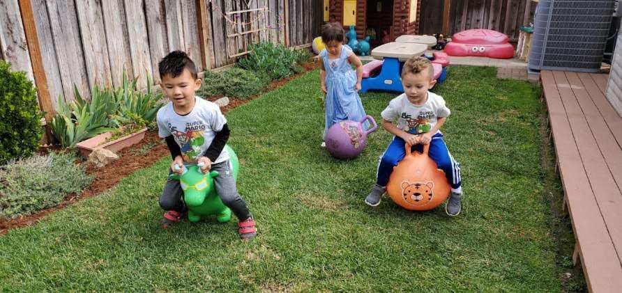 Three children playing with bouncy toys in a grassy yard