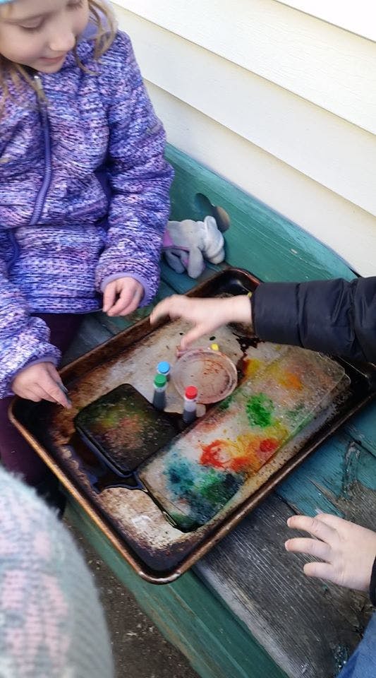 Children playing with colored ice on a baking sheet