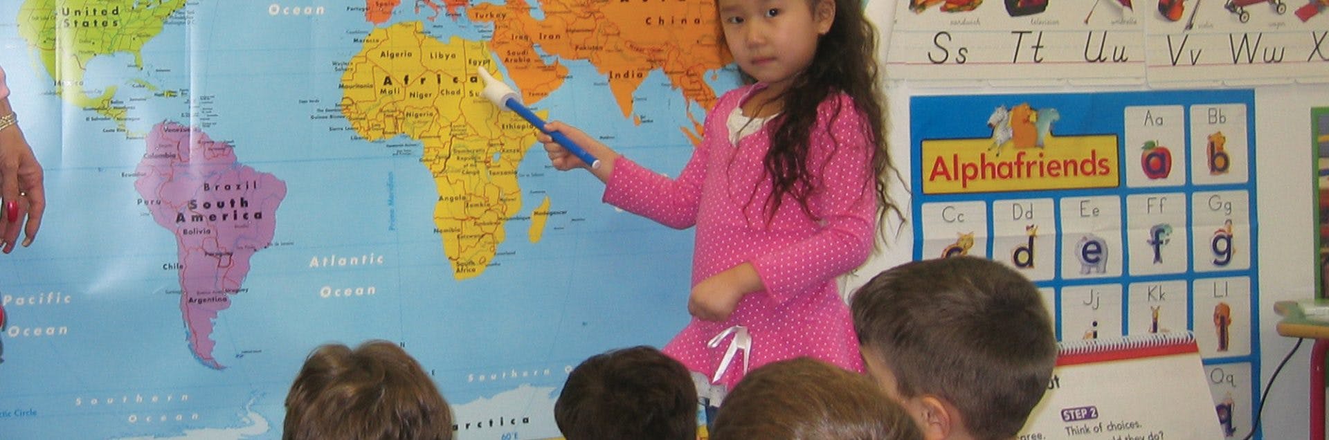Child pointing at a world map with a pointer in a classroom