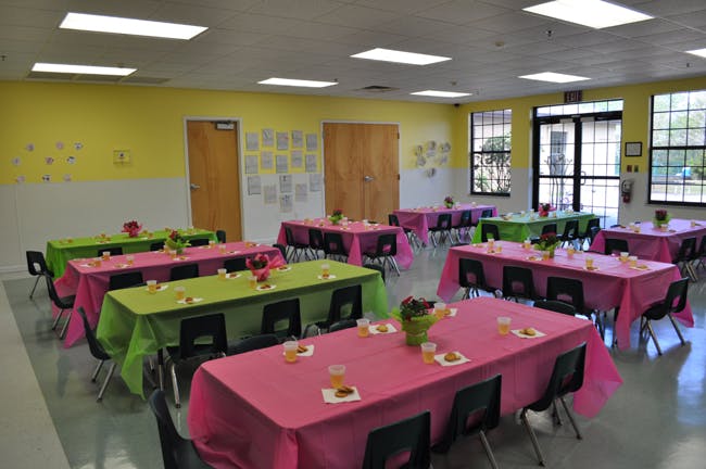 Room with multiple tables covered in pink and green tablecloths