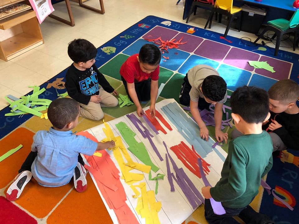 Children on a colorful rug working on a large art project