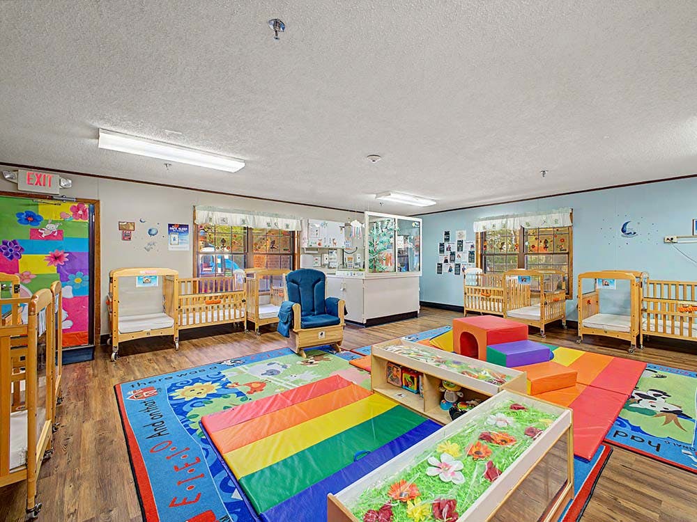 A colorful childcare classroom with cribs, play mats, and a blue rocking chair
